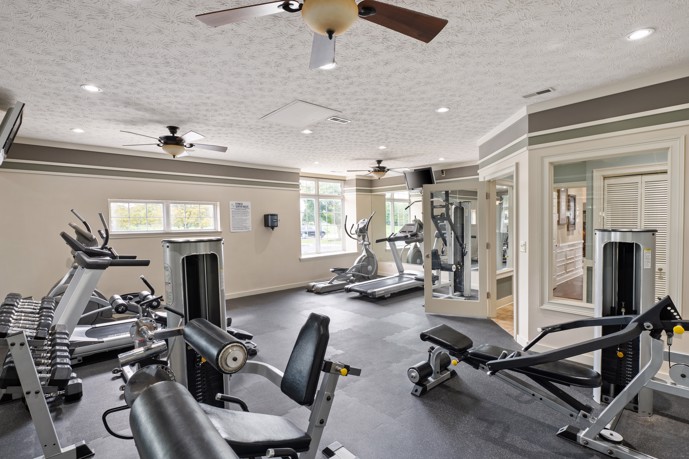 Fitness center showcasing large windows, cardio, and weight equipment, along with an entrance to the clubhouse and ceiling fans.